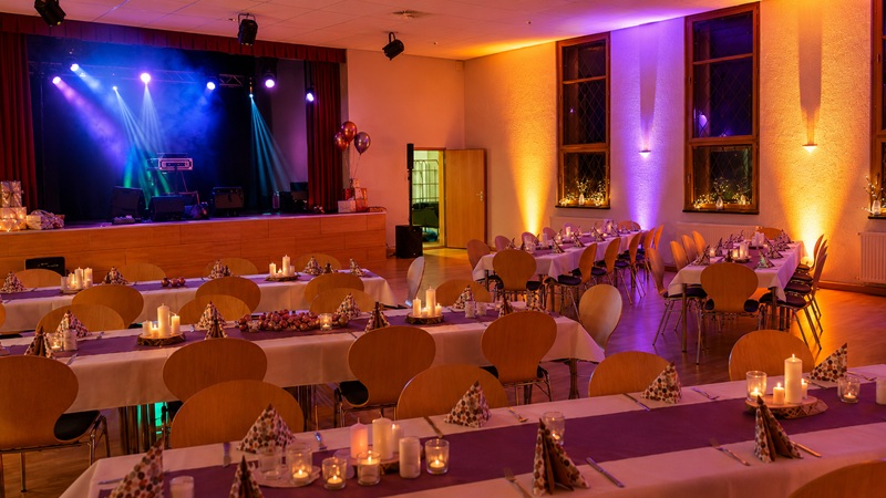 Abendlich beleuchteter Festsaal Zur Katze mit Bühne und gedeckten Tischen